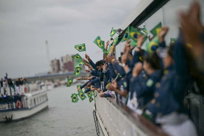 Atletas da delegação brasileira agitam bandeiras brasileiras enquanto navegam em um barco pelo rio Sena no início da cerimônia de abertura dos Jogos Olímpicos de Paris 2024, em Paris, no dia 26 de julho de 2024 -  (crédito: CARL DE SOUZA / POOL / AFP)