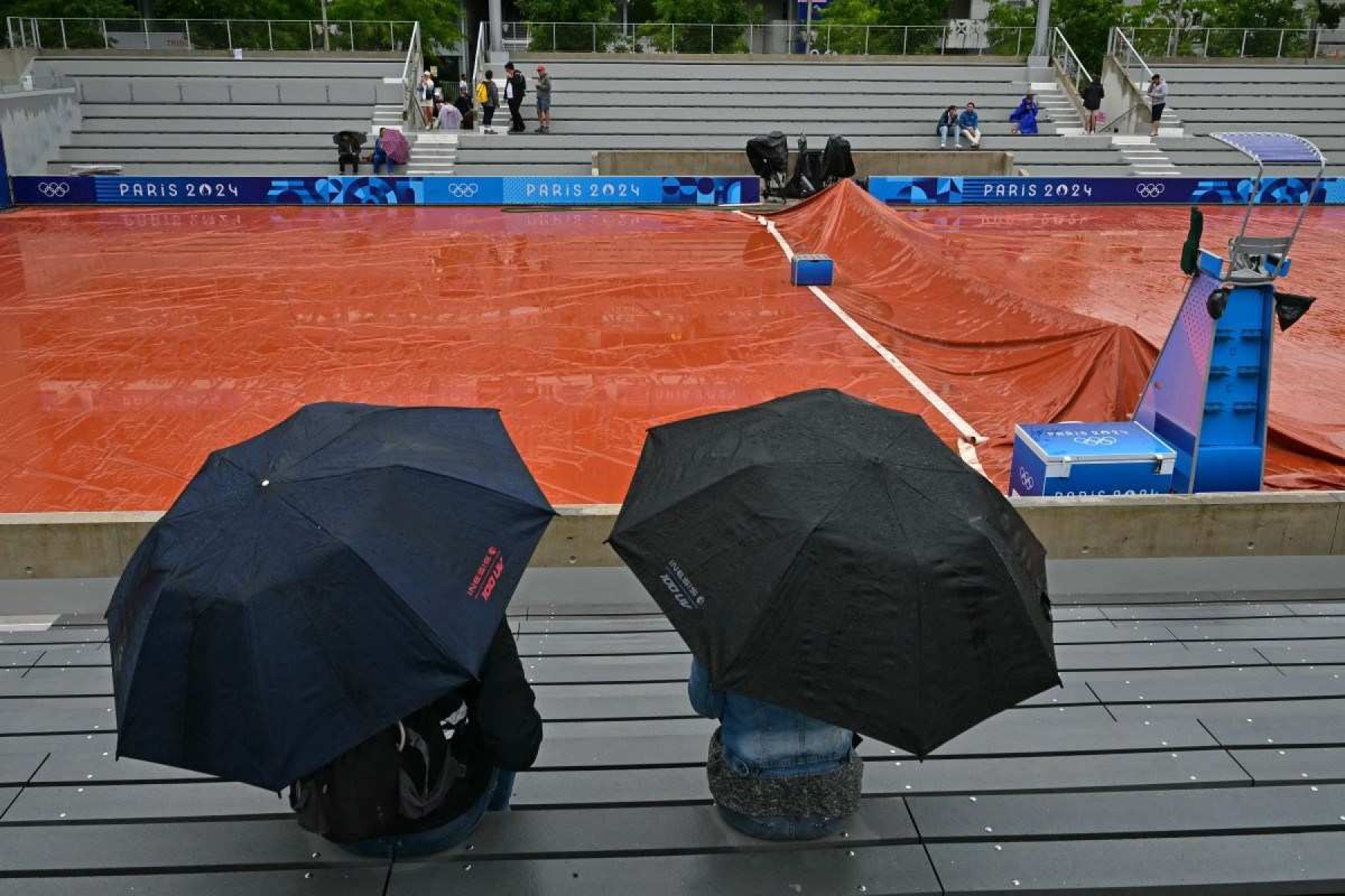 Espectadores se protegem da chuva enquanto a chuva atrasa o início dos jogos nas quadras externas do Estádio Roland-Garros dos Jogos Olímpicos Paris 2024, em Paris, no dia 27 de julho de 2024.