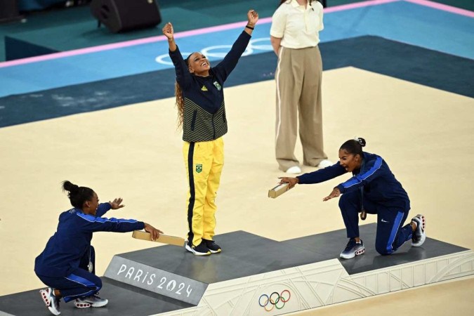 Rebeca Andrade no pódio sendo reverenciada por Simone Biles e Jordan Chiles             -  (crédito: Paul ELLIS / AFP)