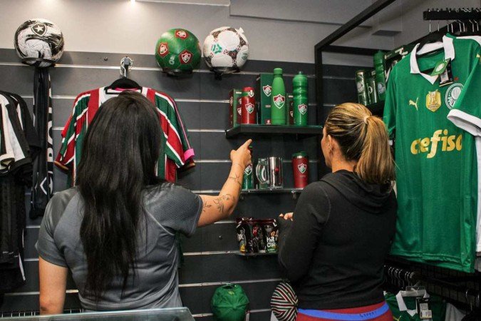 Camila Oliveira escolhendo o presente do pai com a ajuda de Eduarda Freitas, atendente na loja de artigos esportivos.