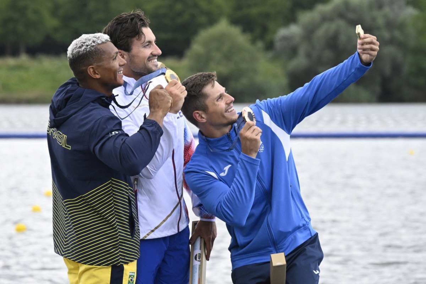 (Da esquerda para a direita) O medalhista de prata do Brasil Isaquias Guimarães Queiroz, o medalhista de ouro da República Tcheca Martin Fuksa e o medalhista de bronze da Moldávia Serghei Tarnovschi comemoram no pódio durante a cerimônia de medalhas após a final dos 1000 m de canoagem individual masculina da competição de canoagem velocidade no Estádio Náutico de Vaires-sur-Marne em Vaires-sur-Marne durante os Jogos Olímpicos de Paris 2024, em 9 de agosto de 2024.      