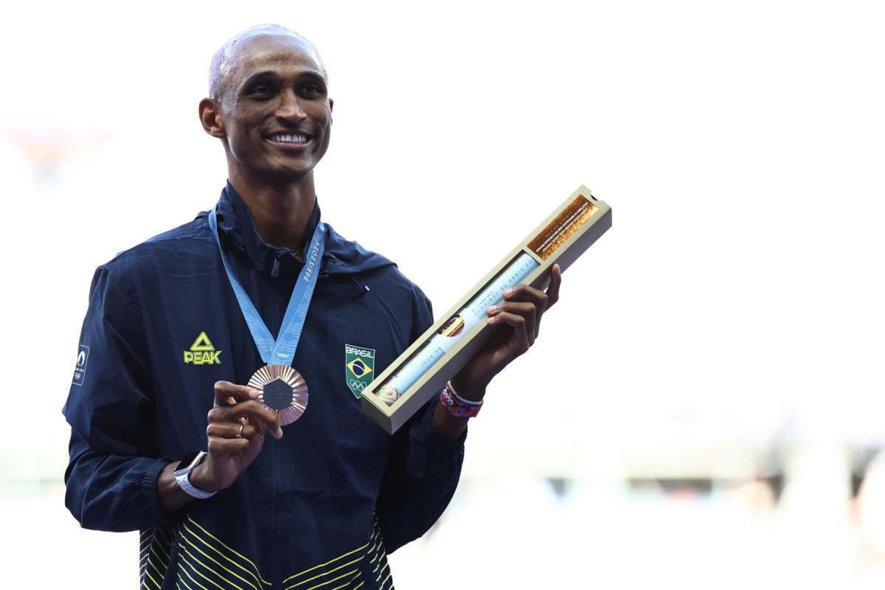 O brasileiro Alison Dos Santos, medalhista de bronze, comemora no pódio durante a cerimônia de vitória da prova masculina de atletismo dos 400m com barreiras durante os Jogos Olímpicos de Paris 2024, no Stade de France, em Saint-Denis, ao norte de Paris, em 10 de agosto de 2024. 