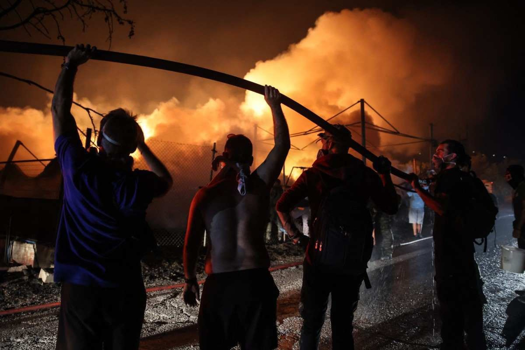  Volunteers hold a water hose in order to help firefighters extinguish a fire in a wood factory in Vrilissia, on the outskirts of Athens, on August 12, 2024. Greeces civil protection authorities ordered the evacuation of several towns in the north-eastern suburbs of Athens, threatened by a violent fire that started the day before and is spreading. European Union said that four countries -- Italy, France, the Czech Republic and Romania -- would send assistance at the request of Greece which is combating a massive wildfire burning through Athens suburbs. (Photo by Aris Oikonomou / AFP)       