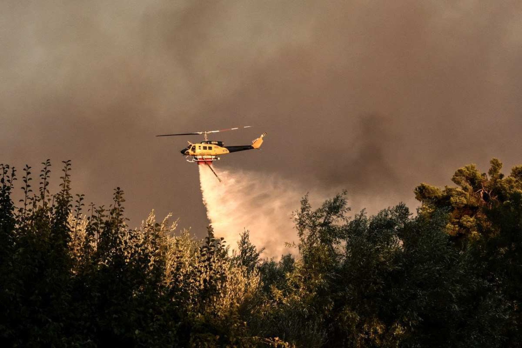  A helicopter drops a load of water over houses during a wildfire in Varnavas, north of Athens, on August 11, 2024. Greece was battling several wildfires on August 11, with smoke covering parts of the capital Athens in a haze, amid warnings for extreme weather conditions for the rest of the week. (Photo by Angelos TZORTZINIS / AFP)       