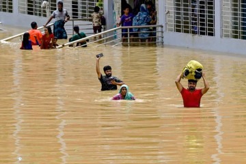 Pessoas atravessam as águas das enchentes fora de um abrigo temporário em Feni, em 24 de agosto de 2024. Quase 300 mil bangladeshianos estão se refugiando em abrigos de emergência em 24 de agosto. -  (crédito: Munir UZ ZAMAN / AFP)