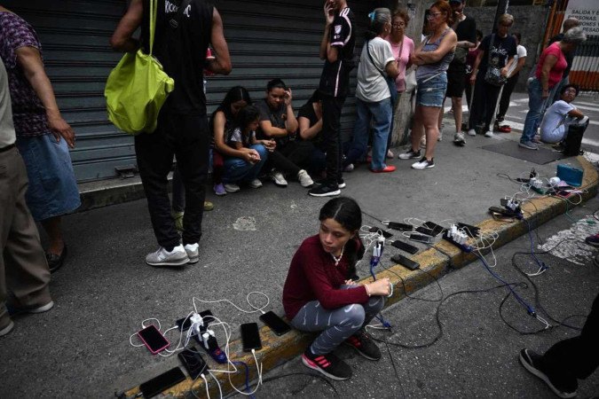 Moradores do bairro de Chacao, em Caracas, carregam celulares usando bateria de caminhão, na calçada  -  (crédito: Juan Barreto/AFP)