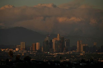 Plumas de fumaça de incêndios florestais são vistas nas montanhas atrás do horizonte do centro de Los Angeles ao pôr do sol -  (crédito: Patrick T. Fallon / AFP)