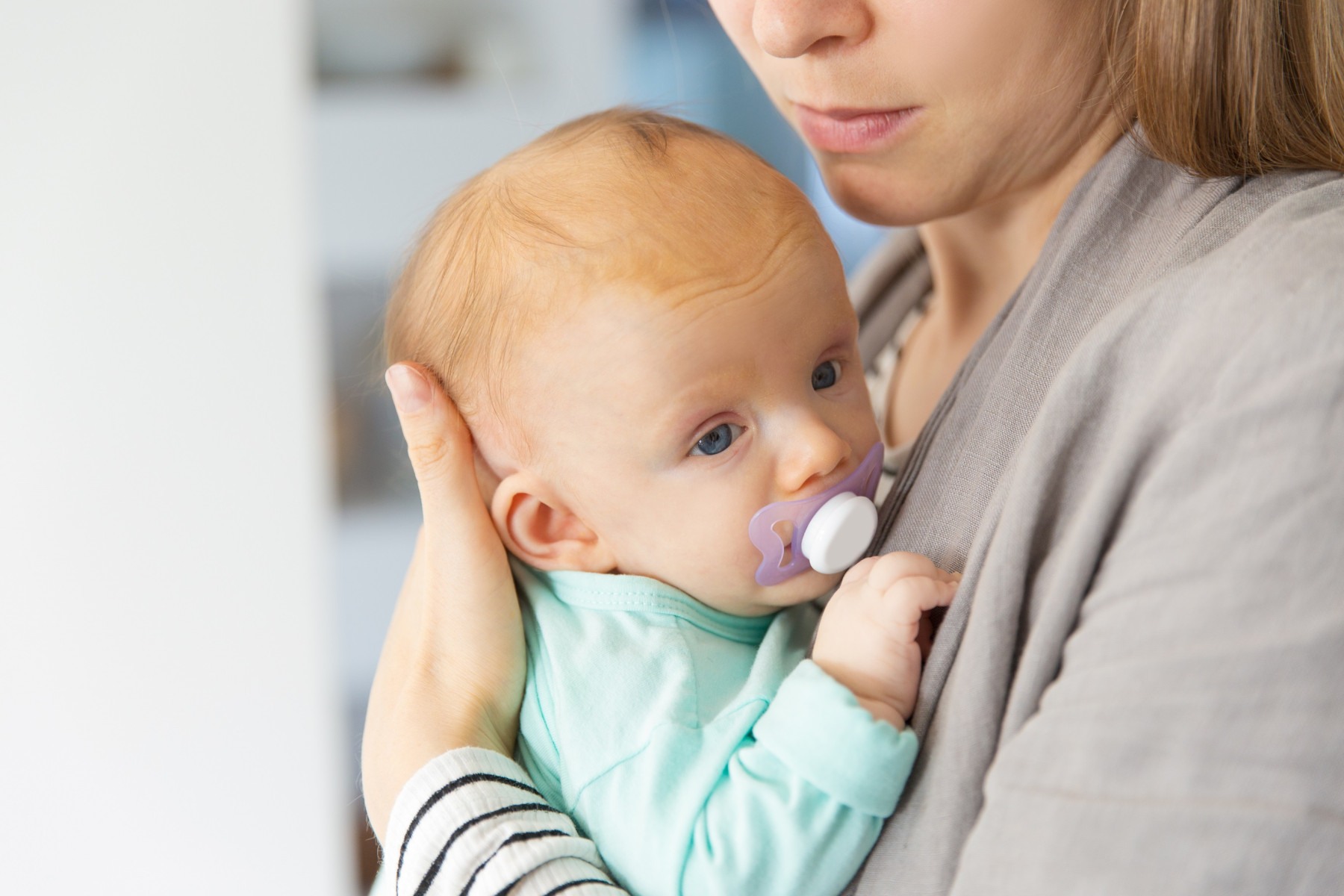  Closeup of cute adorable red haired baby with soother in mothers arms. Portrait of young woman and cute little child in home interior. Happy new mom concept
     -  (crédito:  Goncalo Costa)