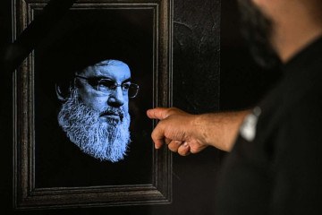 Libanês aponta para a tela de televisão anunciando o assassinato de Hassan Nasrallah, com imagem coberta por faixa preta de luto  -  (crédito: Joseph Eid/AFP)