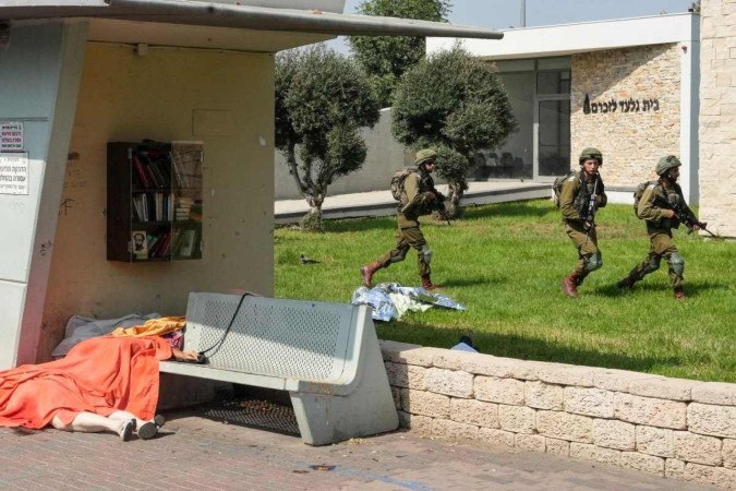 Soldados israelenses patrulham a cidade de Sderot, no sul de Israel, diante de corpos de vítimas do Hamas