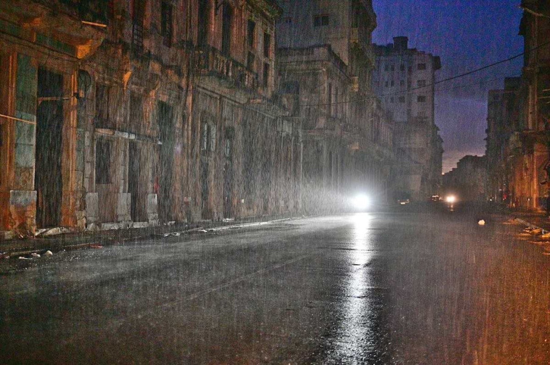     Uma motocicleta ilumina uma rua sob chuva torrencial durante um apagão nacional causado por uma falha na rede em Havana, em 19 de outubro de 2024. Avarias técnicas, escassez de combustível e alta demanda fizeram com que as usinas termelétricas do país falhassem constantemente, forçando o governo a declarar uma emergência energética e tomar medidas como o encerramento de escolas e fábricas. (Foto de ADALBERTO ROQUE/AFP)       