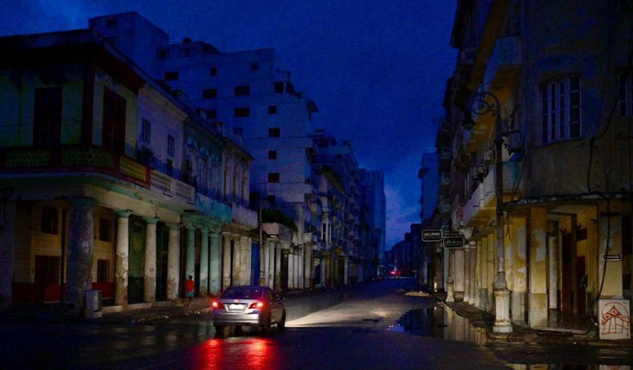     Um carro circula por uma rua durante um apagão nacional causado por uma falha na rede em Havana, em 19 de outubro de 2024. Avarias técnicas, escassez de combustível e alta demanda fizeram com que as usinas termelétricas do país falhassem constantemente, forçando o governo a declarar uma declaração de energia. fornecer emergência e tomar medidas como fechar escolas e fábricas. (Foto de ADALBERTO ROQUE/AFP)       