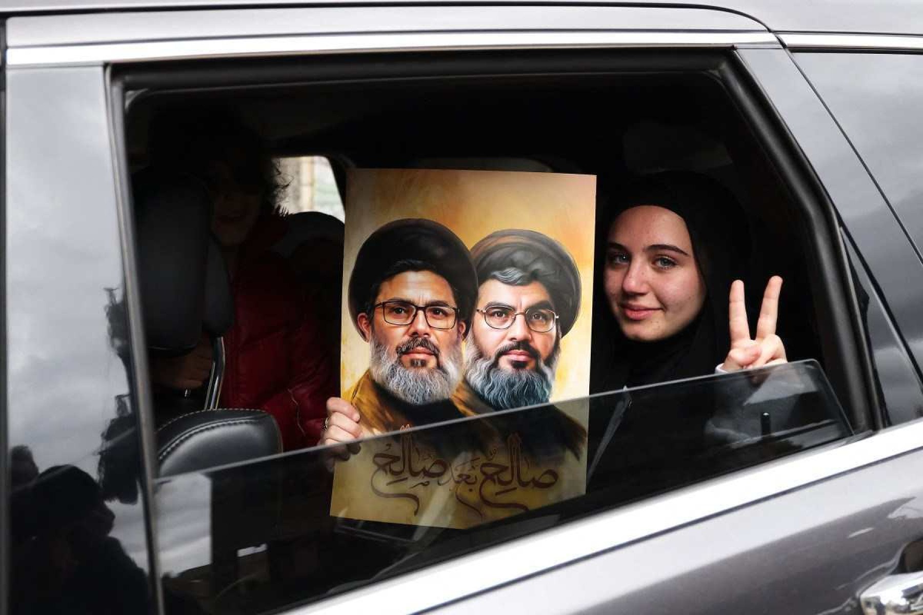 Mulher faz sinal de vitória e mostra fotos de Hassan Nasrallah e Hashem Safiedinne, ao chegar na cidade de Qana 