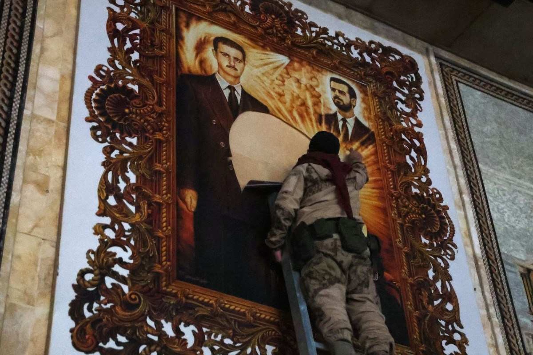 Combatente da oposição rasga cartaz de Bashar Al-Assad (L) e seu irmão Maher, no aeroporto de Aleppo 