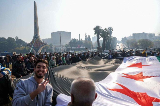 Moradores de Damasco celebram a queda de Al-Assad com uma grande bandeira da oposição síria, na Praça Umayyad  -  (crédito: Omar Haj Kadour/AFP)