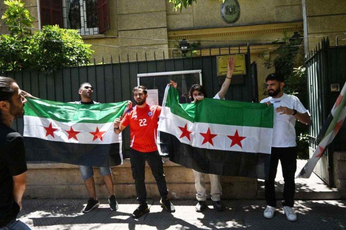     Cidadãos sírios que vivem no Chile comemoram com bandeiras da oposição síria a queda do presidente sírio Bashar al-Assad em frente à sua embaixada em Santiago, em 10 de dezembro de 2024. (Foto de RODRIGO ARANGUA/AFP) Legenda 