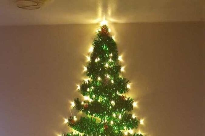 Quem tem crianças pequenas que ainda não entendem ou podem participar, mas quer manter a árvore mais segura, pode investir nessa opção feita com fitas de folhas e luzes na parede 