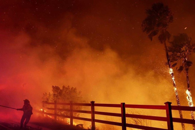 Um bombeiro puxa uma mangueira de água enquanto o Franklin Fire queima palmeiras em Malibu, na Califórnia       -  (crédito: MARIO TAMA / GETTY IMAGES NORTH AMERICA / GETTY IMAGES VIA AFP)