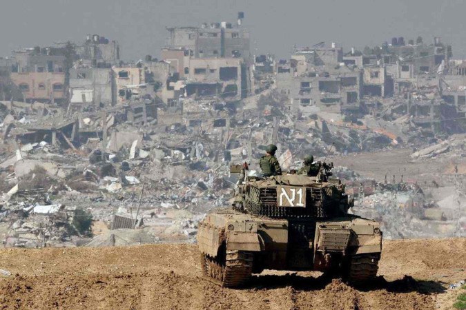 Um tanque israelense mantém posição no sul do país, na fronteira com Gaza, diante de edifícios devastados 