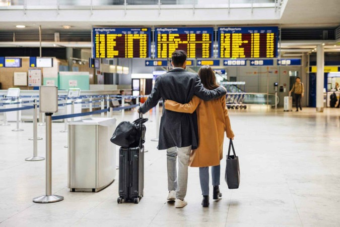  A couple walks hand in hand through the airport departure hall, with the flight information display boards in the background, signaling the start of a new journey.
     -  (crédito:  Hinterhaus Productions)