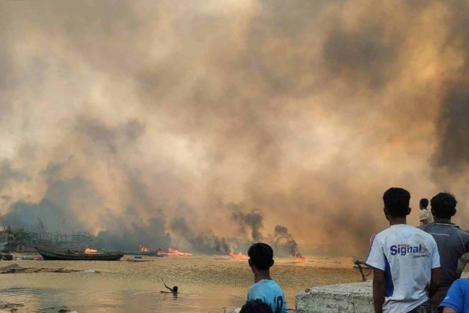 Pessoas olhando para casas em chamas no local de um  ataque aéreo realizado pelos militares de Mianmar -  (crédito: Handout / Arakan Army/ AFP)