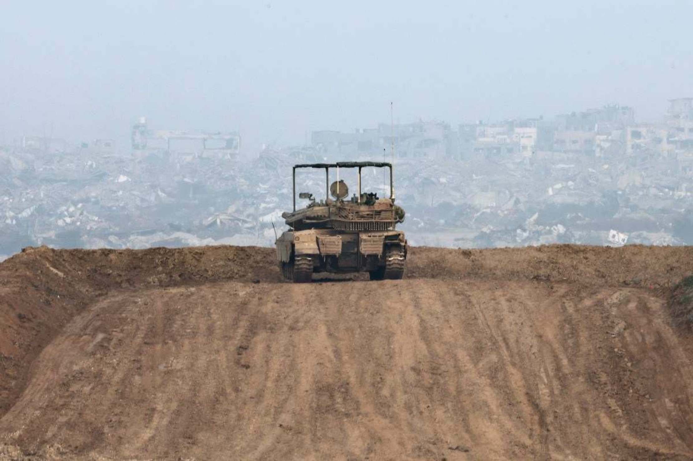 Tanque israelita estacionado numa colina, em frente a edifícios destruídos no norte da Faixa de Gaza 