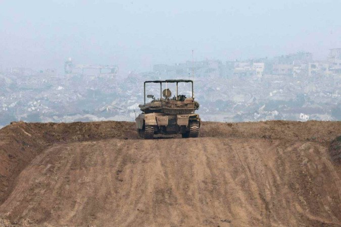 Tanque israelita estacionado numa colina, em frente a edifícios destruídos no norte da Faixa de Gaza 