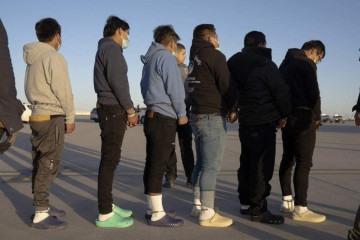 Imigrantes ilegais acorrentados aos pés fazem uma fila para embarcar em uma aeronave militar em Fort Bliss (Texas)