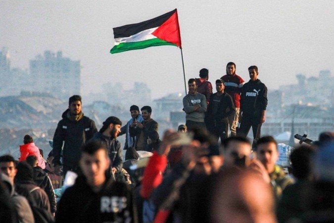 As pessoas esperam pelo retorno dos palestinos deslocados que passam pela rua costeira al-Rashid de Gaza depois de cruzar o corredor Netzarim do sul da Faixa de Gaza ao norte até a Cidade de Gaza em 27 de janeiro de 2025      