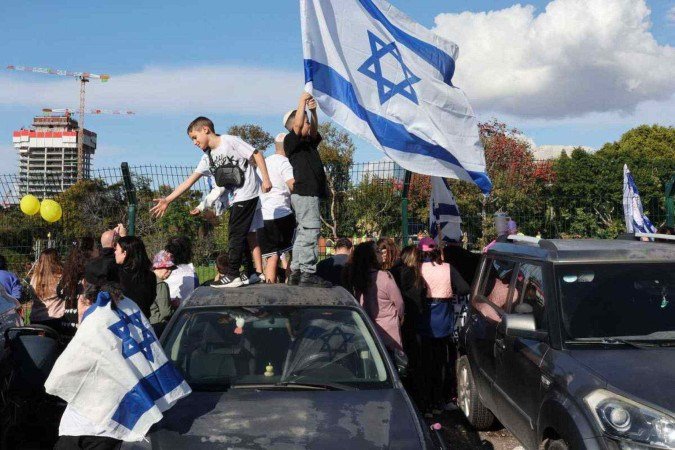 Pessoas agitam bandeiras nacionais em frente ao heliponto do Hospital Beilinson, em Petah Tikva, em 25 de janeiro de 2025, enquanto aguardam a chegada de reféns israelenses libertados por militantes do Hamas - (crédito: Jack GUEZ / AFP) Pessoas agitam bandeiras nacionais em frente ao heliponto do Hospital Beilinson, em Petah Tikva, em 25 de janeiro de 2025, enquanto aguardam a chegada de reféns israelenses libertados por militantes do Hamas - (crédito: Jack GUEZ / AFP)