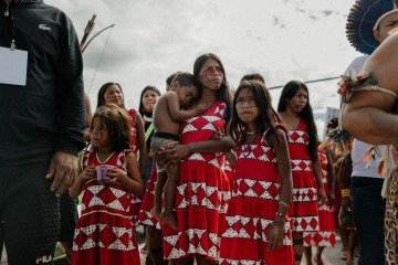 Uma mulher Maxacali caminha sob o sol com suas filhas durante o Acampamento Terra Livre 