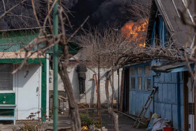 Um morador local (C) observa um incêndio do pátio de sua casa após um ataque nos arredores de Odessa, em 11 de março de 2025, em meio à invasão russa da Ucrânia       -  (crédito: Oleksandr GIMANOV / AFP)