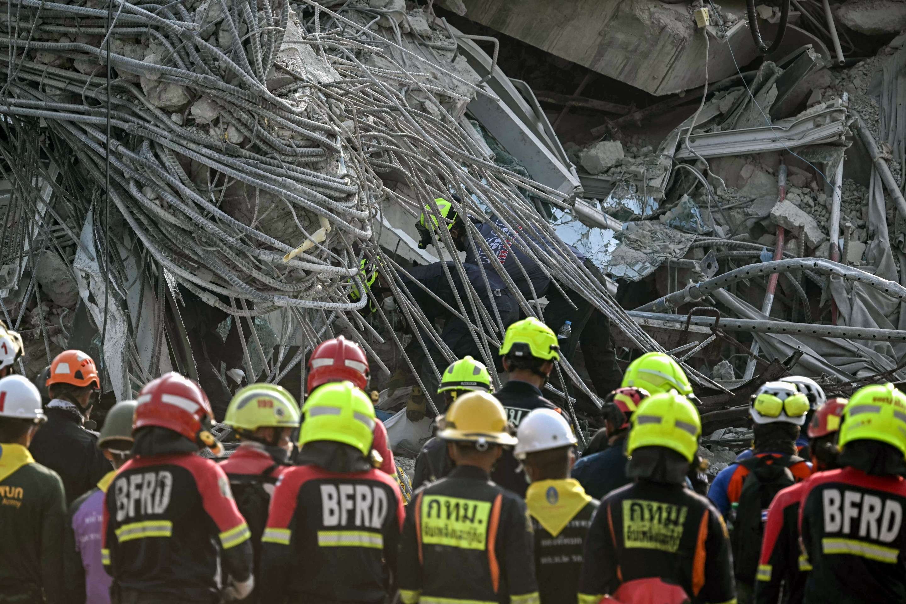  Equipes de resgate observam enquanto o corpo de uma vítima é extraído dos escombros no local do desabamento de um prédio em construção em Bangkok em 29 de março de 2025, um dia após um terremoto atingir o centro de Mianmar e a Tailândia. O número de mortos em um grande terremoto que atingiu Mianmar e a Tailândia passou de 1.000 em 29 de março, enquanto equipes de resgate cavavam os escombros de prédios desabados em uma busca desesperada por sobreviventes. (Foto de Lillian SUWANRUMPHA / AFP)       