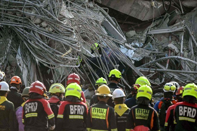  Equipes de resgate observam enquanto o corpo de uma vítima é extraído dos escombros no local do desabamento de um prédio em construção em Bangkok em 29 de março de 2025, um dia após um terremoto atingir o centro de Mianmar e a Tailândia. O número de mortos em um grande terremoto que atingiu Mianmar e a Tailândia passou de 1.000 em 29 de março, enquanto equipes de resgate cavavam os escombros de prédios desabados em uma busca desesperada por sobreviventes. (Foto de Lillian SUWANRUMPHA / AFP)       
