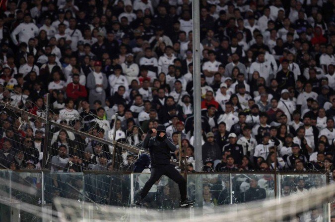 Torcedor mascarado do Colo-Colo se equilibra na cerca que separa a torcida do gramado 