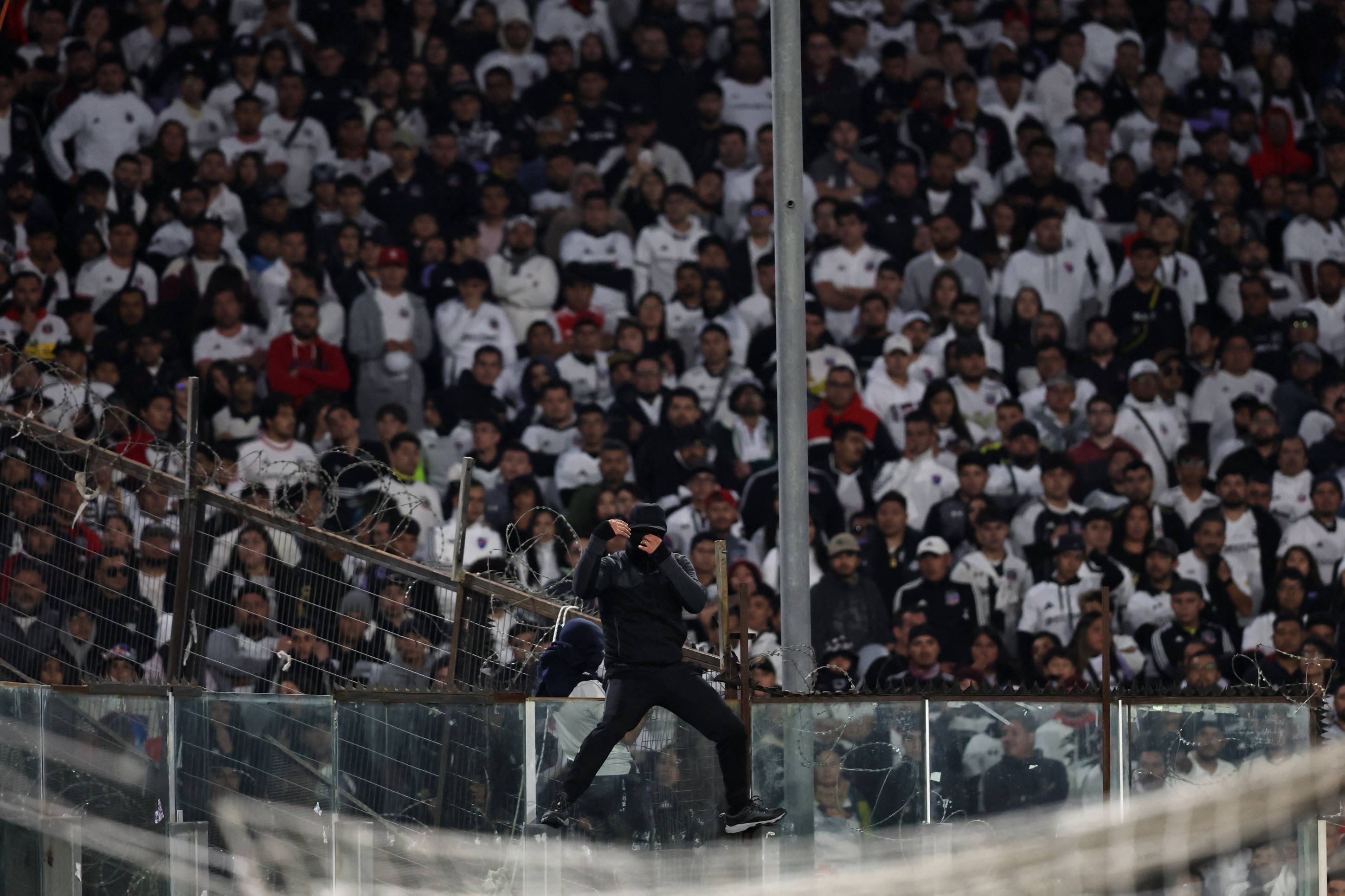 Torcedor mascarado do Colo-Colo se equilibra na cerca que separa a torcida do gramado 