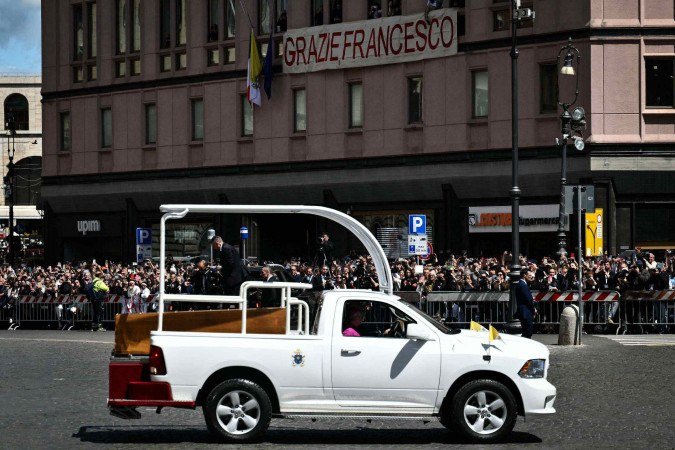 Participantes observam a chegada do carro fúnebre carregando o caixão do falecido Papa Francisco perto da Basílica de Santa Maria Maggiore, seu local de descanso final, com uma faixa com os dizeres 