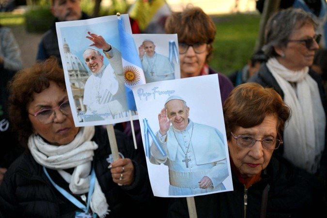 Fiéis católicos seguram cartazes com imagens do Papa Francisco em frente à Catedral de Buenos Aires, em 26 de abril de 2025