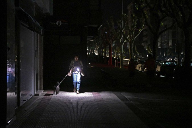 Mulher usa celular para iluminar caminhada nas ruas de Vigo, na Espanha, com cachorro em meio ao apagão de ontem que atingiu vários países  -  (crédito:  AFP)