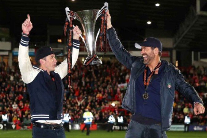 WREXHAM, WALES - APRIL 22: Rob McElhenney and Ryan Reynolds, Owners of Wrexham celebrate with the Vanarama National League trophy as Wrexham win the Vanarama National League and are promoted to the English Football League after victory in the Vanarama National League match between Wrexham and Boreham Wood at Racecourse Ground on April 22, 2023 in Wrexham, Wales. (Photo by Jan Kruger/Getty Images)
- (crédito: Getty Images) WREXHAM, WALES - APRIL 22: Rob McElhenney and Ryan Reynolds, Owners of Wrexham celebrate with the Vanarama National League trophy as Wrexham win the Vanarama National League and are promoted to the English Football League after victory in the Vanarama National League match between Wrexham and Boreham Wood at Racecourse Ground on April 22, 2023 in Wrexham, Wales. (Photo by Jan Kruger/Getty Images)
- (crédito: Getty Images)
