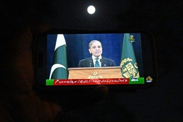 Um morador observa seu smartphone enquanto o primeiro-ministro paquistanês, Shehbaz Sharif, discursa à nação em Islamabad, em 10 de maio de 2025 -  (crédito: Aamir QURESHI/AFP)