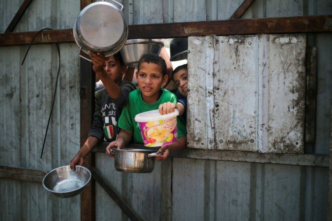 Crianças palestinas mostram vasilhas e potes vazios, enquanto esperam por comida, em Nuseirat - (crédito: Eyad Baba/AFP) Crianças palestinas mostram vasilhas e potes vazios, enquanto esperam por comida, em Nuseirat - (crédito: Eyad Baba/AFP)
