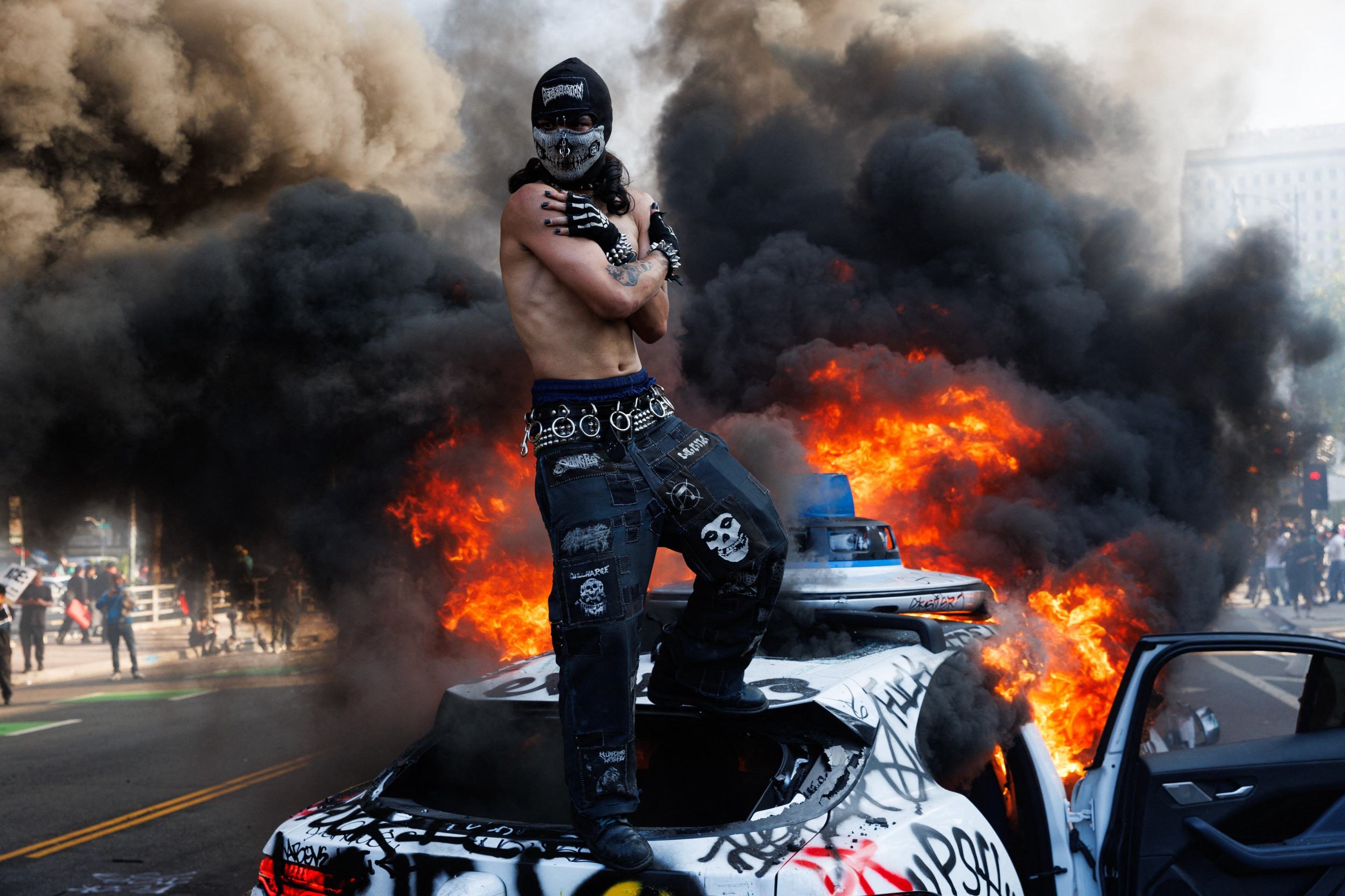 Manifestante mascarado sobre carro autônomo Waymo, depois de atear fogo e pichar o veículo, em Los Angeles, no último domingo  -  (crédito: Blake Flagan/AFP)