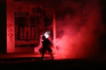 Fogo de artifício explode atrás de policial de choque durante protesto no bairro Little Tokyo, em Los Angeles  -  (crédito: Ronald Schemidt/AFP)