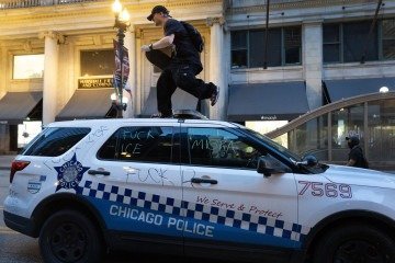 Homem sobre viatura da polícia pichada com frases, como 