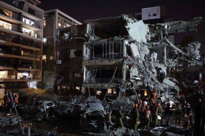 Israeli troops and first responders gather in front of a building hit by a missile fired from Iran, in Ramat Gan near Tel Aviv on June 13, 2025. Iran fired a barrage of ballistic missiles at Israel in a counter-strike in the evening on June 13, after an unprecedented onslaught hammered the Islamic republic's top military brass and targeted its nuclear facilities and bases. (Photo by Jack GUEZ / AFP)
- (crédito: AFP) Israeli troops and first responders gather in front of a building hit by a missile fired from Iran, in Ramat Gan near Tel Aviv on June 13, 2025. Iran fired a barrage of ballistic missiles at Israel in a counter-strike in the evening on June 13, after an unprecedented onslaught hammered the Islamic republic's top military brass and targeted its nuclear facilities and bases. (Photo by Jack GUEZ / AFP)
- (crédito: AFP)