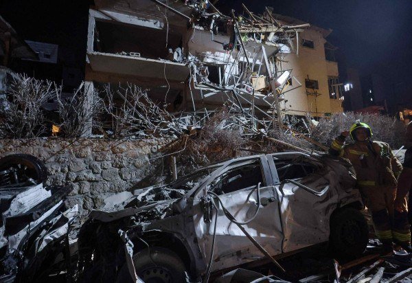 Um bombeiro israelense está ao lado de um carro destruído em um local atingido por um míssil disparado do Irã, em Ramat Gan, nos arredores de Tel Aviv, em 13 de junho de 2025 - (crédito: GIL COHEN-MAGEN / AFP)