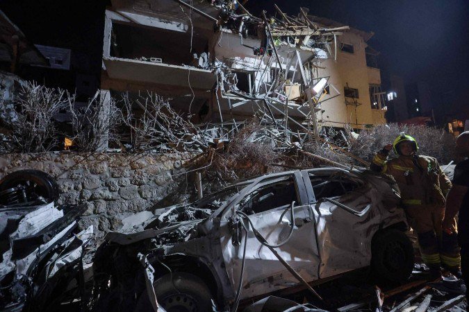 Um bombeiro israelense está ao lado de um carro destruído em um local atingido por um míssil disparado do Irã, em Ramat Gan, nos arredores de Tel Aviv, em 13 de junho de 2025 - (crédito: GIL COHEN-MAGEN / AFP) Um bombeiro israelense está ao lado de um carro destruído em um local atingido por um míssil disparado do Irã, em Ramat Gan, nos arredores de Tel Aviv, em 13 de junho de 2025 - (crédito: GIL COHEN-MAGEN / AFP)