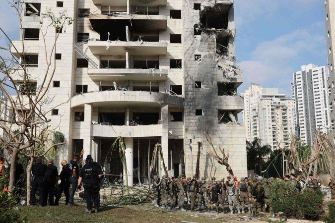 Equipes são vistas ao lado de um prédio danificado após um ataque de um míssil iraniano na cidade israelense de Petah Tikva, a leste de Tel Aviv, em 16 de junho de 2025 - (crédito: Jack GUEZ/AFP) Equipes são vistas ao lado de um prédio danificado após um ataque de um míssil iraniano na cidade israelense de Petah Tikva, a leste de Tel Aviv, em 16 de junho de 2025 - (crédito: Jack GUEZ/AFP)