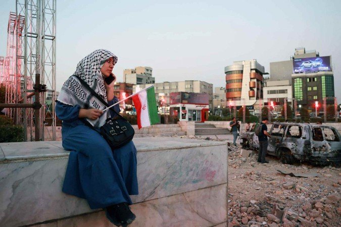 Iraniana senta-se diante de carro destruído pelos ataques, em Teerã